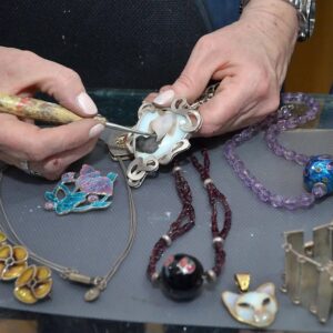 Una mujer trabaja en un collar usando un cuchillo, concentrada en su tarea creativa.