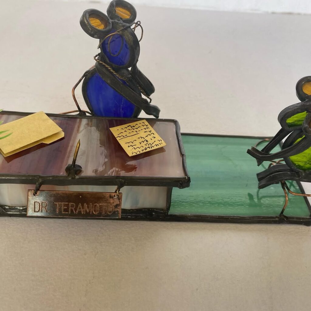 Escultura de vidrio y metal de dos ratones sobre un escritorio.