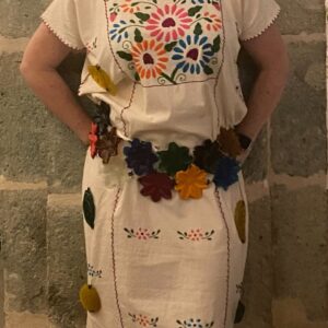 Mujer con vestido mexicano y cinturón de flores, mostrando colores vibrantes y un estilo tradicional.