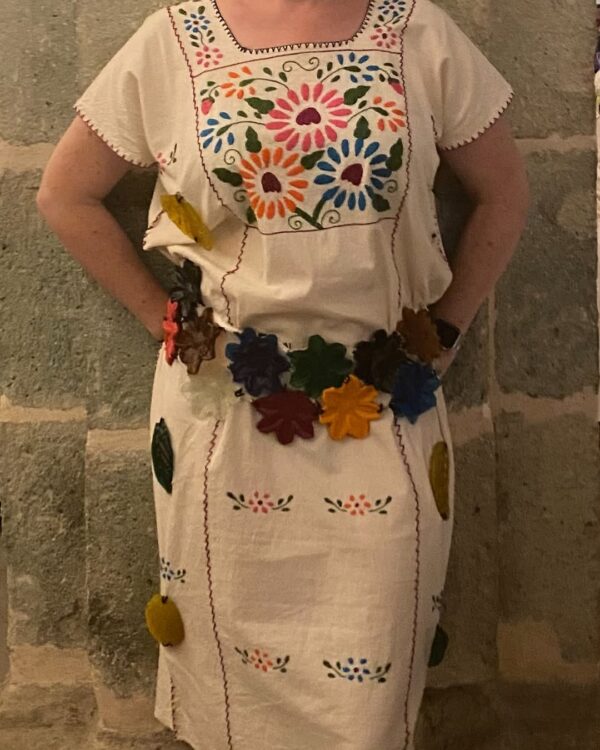 Mujer con vestido mexicano y cinturón de flores, mostrando colores vibrantes y un estilo tradicional.