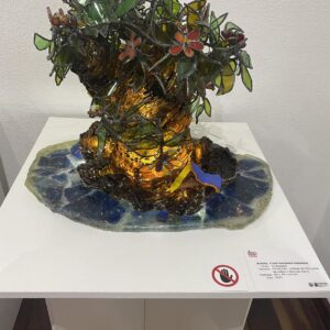 Escultura de vidrio de un árbol con flores y pájaros, mostrando belleza y delicadeza en su diseño.