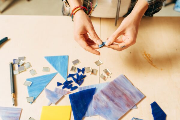 Una persona creando un mosaico colorido con pequeñas piezas de cerámica en una mesa.